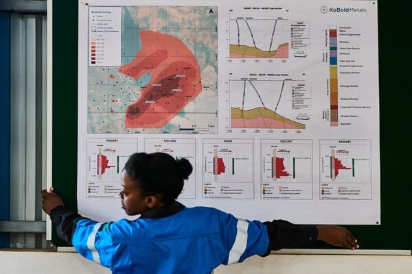 A person in a blue-and-white shirt carries a large map and series of charts.