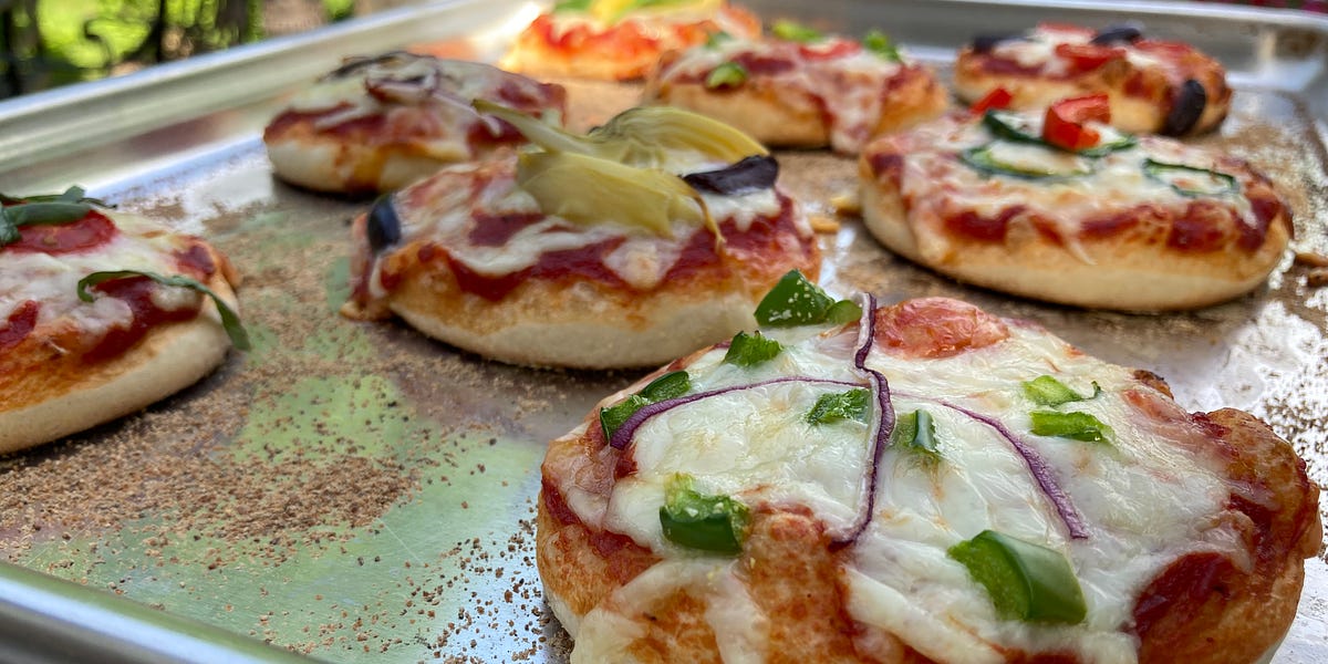Miniature pizza's topped with cheese green pepper, onion and olives on a sheet pan. 