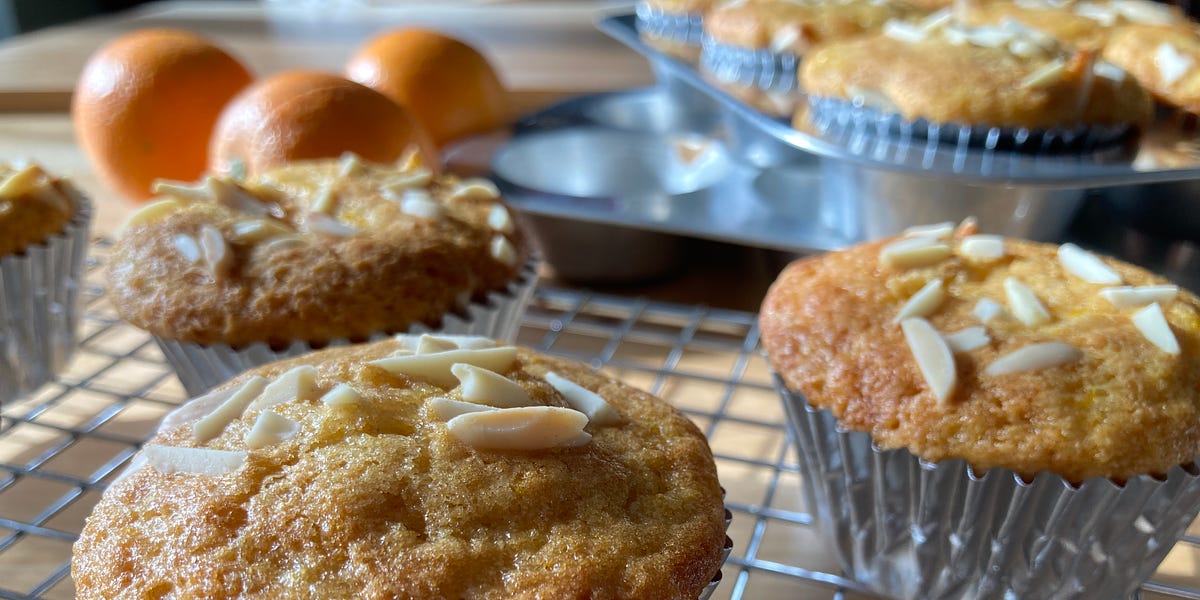 Orange muffins topped with slivered almonds on a wire rack.