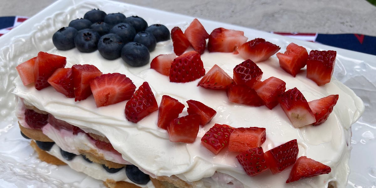 Layered icebox cake topped with white frosting, diced strawberries and blueberries.