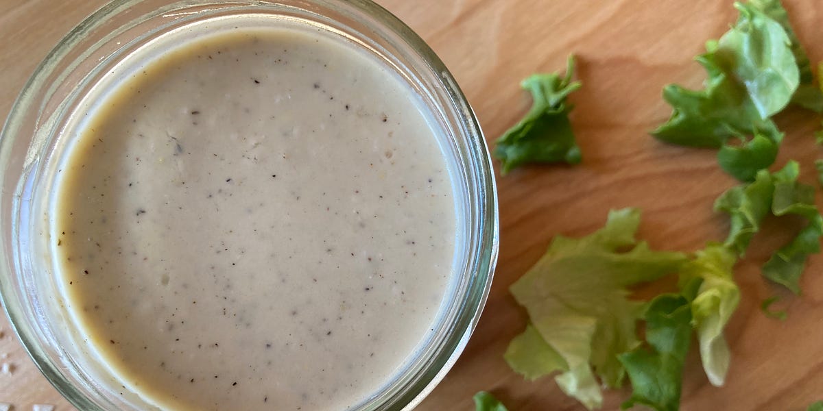 Caesar dressing in a jar on a wood cutting board with cut romaine lettuce.