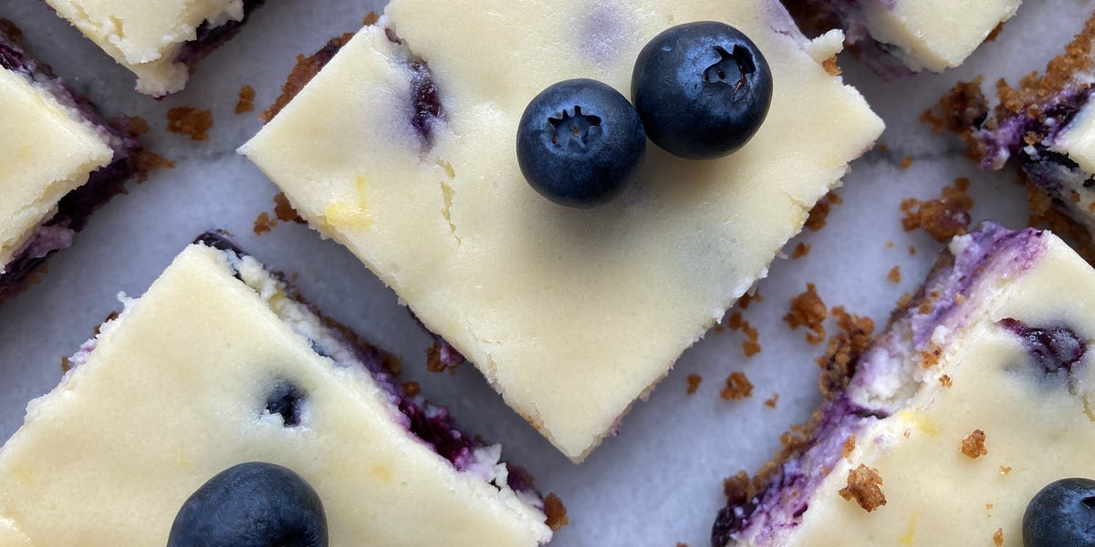 Cheesecake squares topped with fresh blueberries on a white plate.