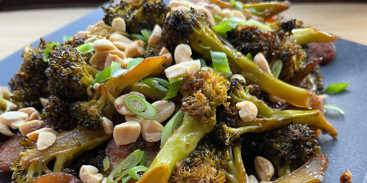Roasted broccoli florets and sliced water chestnuts topped with peanuts on a gray plate.