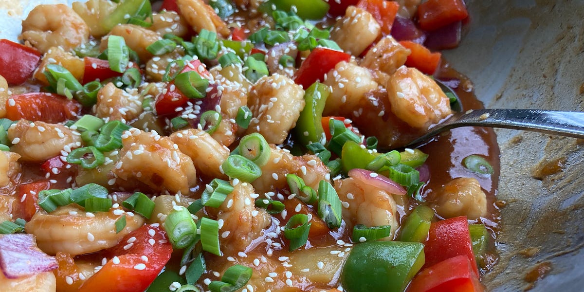 Shrimp, red and green peppers, and red onion in a sweet and sour sauce in a wok.
