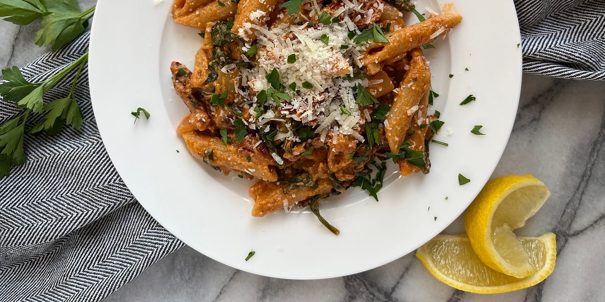 Sun-dried tomato pasta topped with parmesan cheese and minced parsley on a white plate.