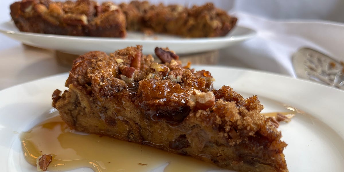 Slice of French toast casserole topped with maple syrup and pecans on a white plate. 