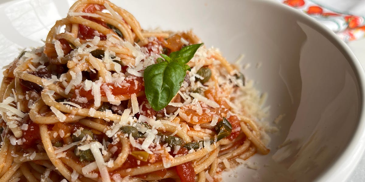 Spaghetti in a red puttanesca sauce topped with grated parmesan cheese in a white bowl.