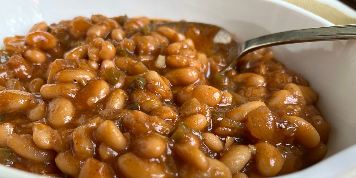 Barbequed baked beans in a white bowl with a serving spoon.
