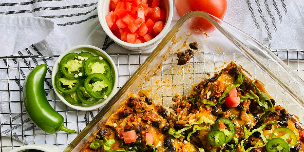 Taco lasagna topped with lettuce, diced tomato and jalapeno slices in a casserole dish.