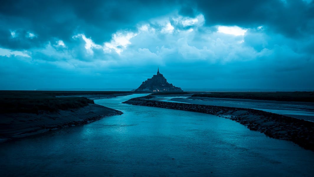  A stormy sea with a castle on a rock in the distance at night with a dark, cloudy sky and choppy water symbolizes the unpredictable nature of future trends in cloud automation.