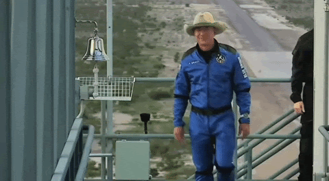 Jeff Bezos, wearing a cowboy hat and a space suit, rings a bell