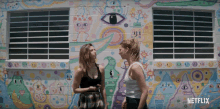 Blair and Sterling standing outside a colorful mural as Blair slouches in complaint