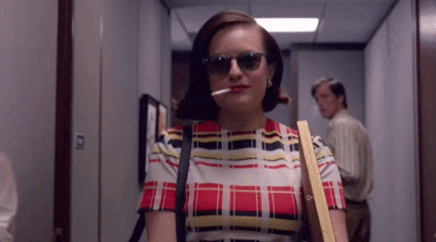 Peggy Olson della serie Mad Men lascia l'ufficio con occhiali da sole e una sigaretta accesa.