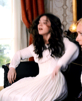 Gif of Hailee Steinfeld as Emily Dickinson in the TV Show "Dickinson" in a white dress, flopping onto a couch.