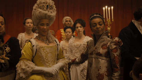Gif of Queen Charlotte in "Bridgerton" wearing a towering white wig and yellow gown, looking at Daphne while she says "She made quite an impression."