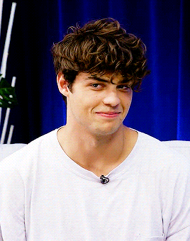 Noah Centineo breaking into laughter in front of a blue curtain. Noah Centineo breaking into laughter in front of a blue curtain.