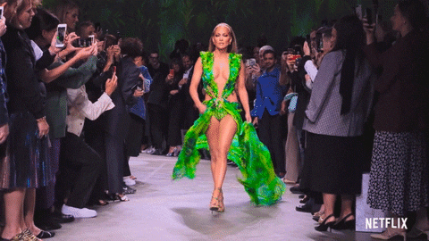 Jennifer Lopez sfila per Versace nel 2020 con l'iconico vestito verde a motivi floreali in stile jungla: lo tiene per i lati e scopre completamente le gambe.