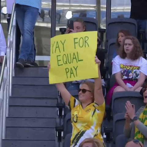 Una donna allo stadio alza un cartello che dice "Yay for equal pay"