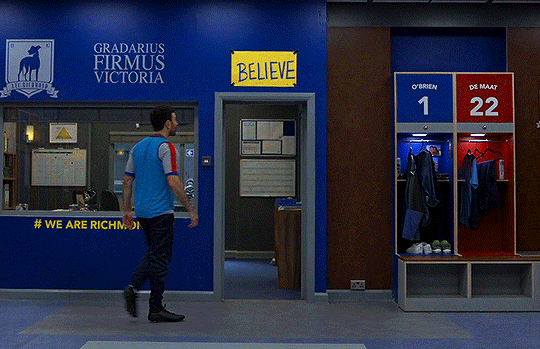 Roy tapping a sign on the wall that says "Believe"