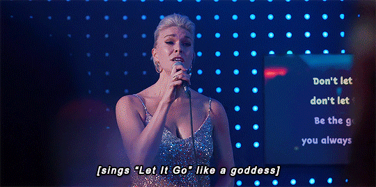 The cast of Ted Lasso at a karaoke bar; Rebecca is singing and the caption reads "[sings "Let it Go" like a goddess]" and then cuts to everyone cheering and the caption reads "[everyone loses their minds]"