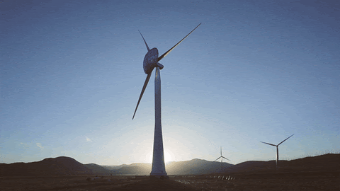 A wind turbine spins; the sun is shining in the background over hills