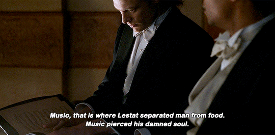 Lestat (to the left) reads sheet music. Louis (to the right) smiles to himself. Caption reads: "Music, that is where Lestat separated man from food. Music pierced his damn soul."