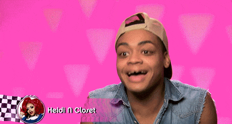 A gif of Heidi N Closet doing a 'confessional' on RuPaul's Drag Race. She is wearing her 'boy clothes' - a denim vest and backwards cap. She is laughing hysterically and clapping like she's just heard a great joke.