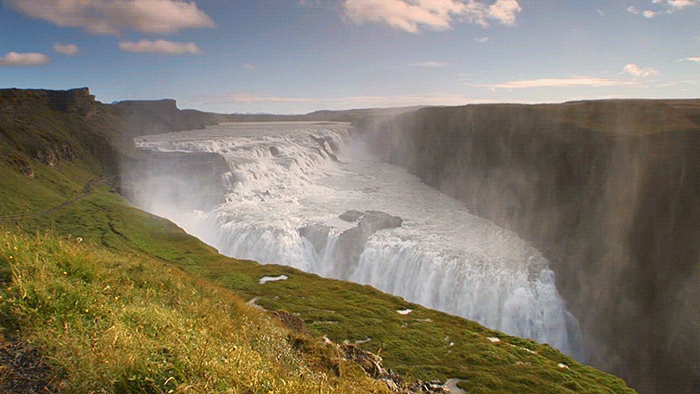 Gif of a large waterfall in Iceland underneath a blue sky. Lower left corner is green expanse.