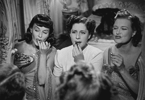 Three women in the movie "The Women" putting on lipstick in a mirror