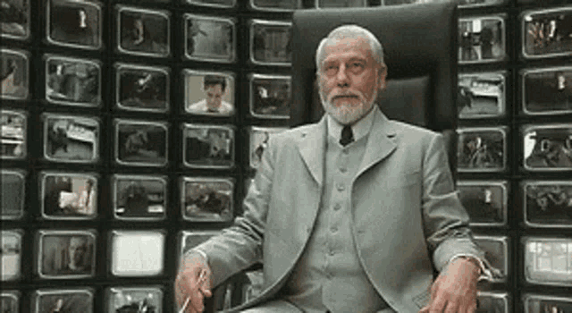 Man with beard sitting in front of a TV wall