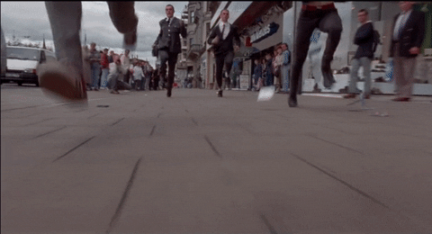 Movie gif. Ewan McGregor as Mark and Ewen Bremner as Spud in Trainspotting run away in a sprint down a busy walkway. 