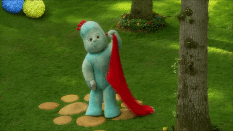 GIF of Igglepiggle, a vaguely human shaped soft toy in pale blue, waving while holding a red blanket