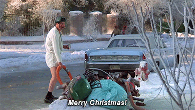Movie gif. Randy Quaid as Cousin Eddie in "National Lampoon's Christmas Vacation stands on a snowy street wearing a short bathrobe, holding a hose near a pile of garbage, and raising up a can of beer. Text, "Merry Christmas!"