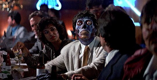 Cena do filme "Eles Vivem", mostrando um alienígena no bar, sem saber que seu rosto alien está à mostra, rodeado por humanos que o observam confusos e assustados.