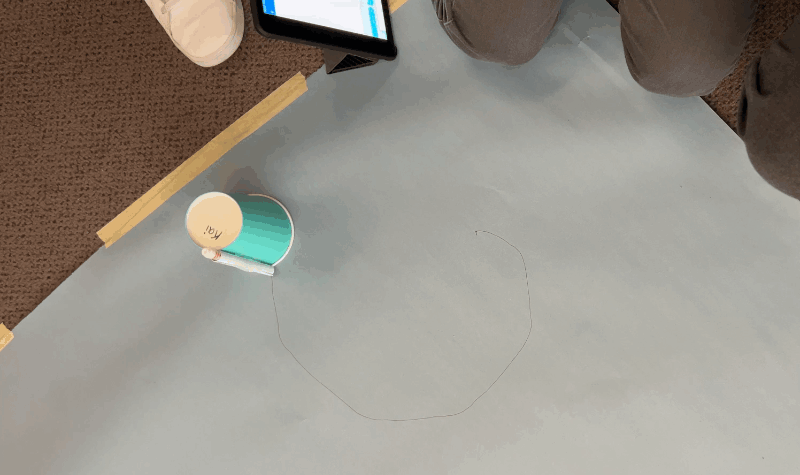 A cup with a marker attached and a Sphero underneath, drawing a circle on paper.