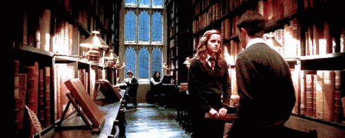 Gif tratta fal film di Harry Potter, dentro alla libreria di Hogwarts, con Hermione Grnager che dà in testa a Harry Potter un rotolo di fogli mentre fuori dalla finestra nevica.