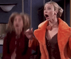 Friends gif. Lisa Kudrow as Phoebe and Jennifer Aniston as Rachel jump up and down, smiling and clapping their hands exuberantly at something offscreen. 