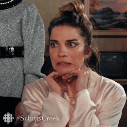 Alexis from Schitt's Creek, is pulling a face. It's like a 'yikes' moment, where she's responding to something off camera, and grimacing her face against her will.