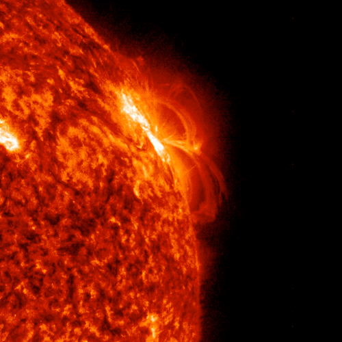 Up close image of the Sun that is a red and orange color against a dark background. A bright flash of yellow erupts from the Sun indicating where the flare occurred.