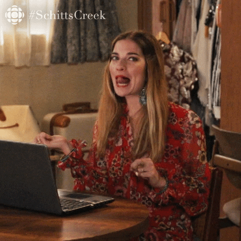 A gif of Alexis from Schitt's Creek flipping her hair multiple times while sticking her tongue out