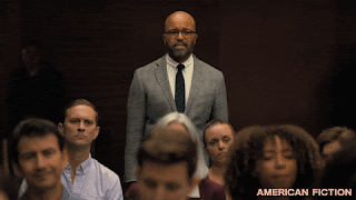 Jeffrey Wright, a black man, is standing at the back of a packed audience. He looks incredulous at what's on stage (unseen to us.) After a second or two, a white woman stand up, directly in front of him, clapping enthusiastically.