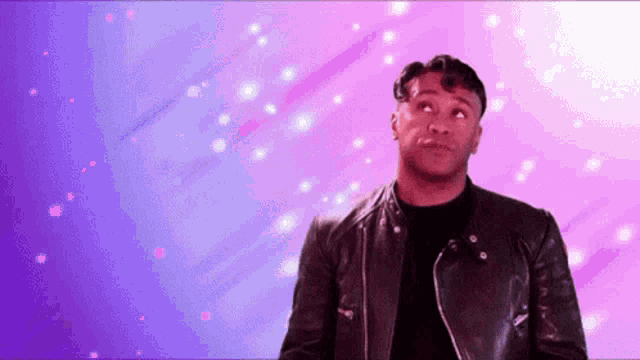 a man in a black leather jacket is standing in front of a purple and pink background .