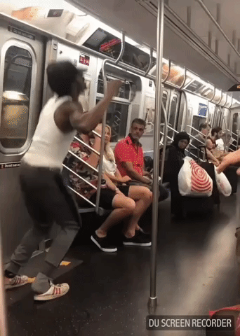 A man does a flip in a New York City subway car, kicking a hat into the air and catching it on his head