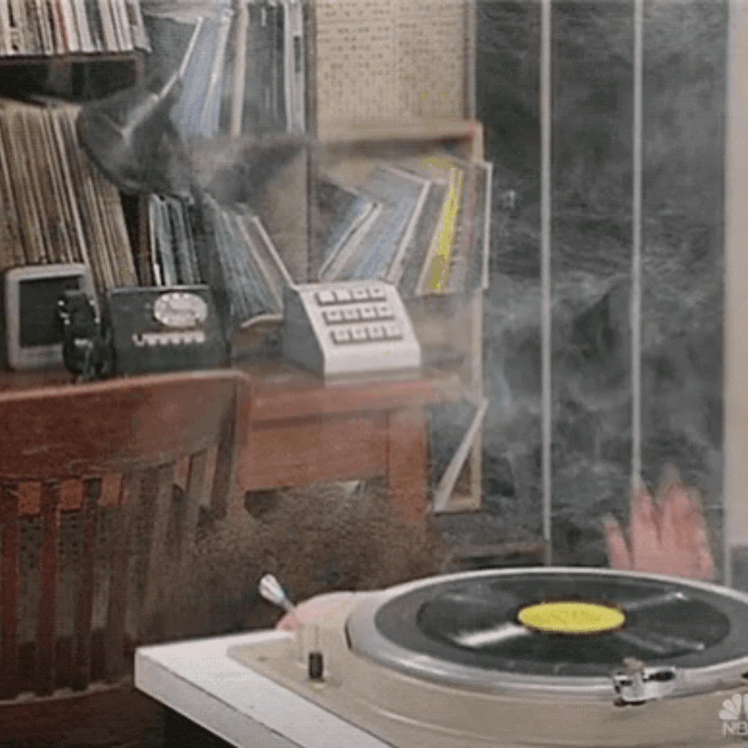 A teenage boy behind a record player with gigantic, frizzy, curly hair standing straight up like he's been electrocuted.