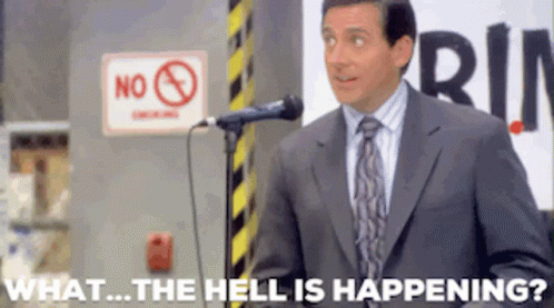 a man in a suit and tie is standing in front of a microphone with the words what the hell is happening behind him