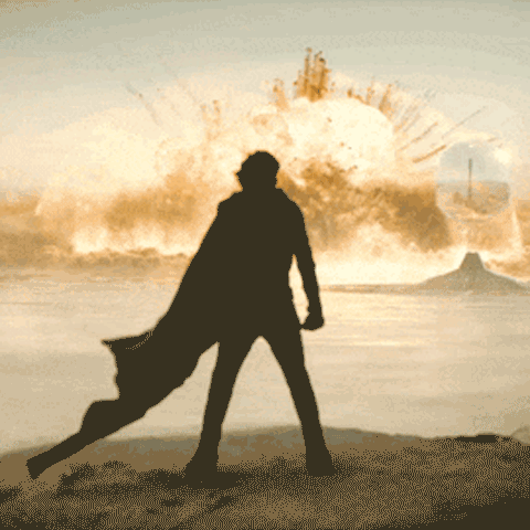  Timothée Chalamet is silhouette, robes flowing behind him, against an enormous explosion some distance away across a desert plain