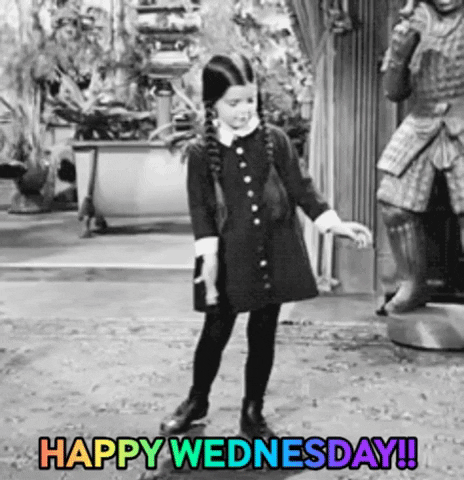 TV gif. In black and white, Wednesday Addams from the original Addams Family dances in her house. She has a happy, but concentrated look on her face as she does a little two step and wiggle of the arms. The rainbow flashing text at the bottom says, “Happy Wednesday!!” 