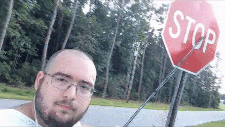 Video gif. A man standing next to a stop sign taps on the sign with an extendable teacher's pointer, indicating that he would like us to stop.
