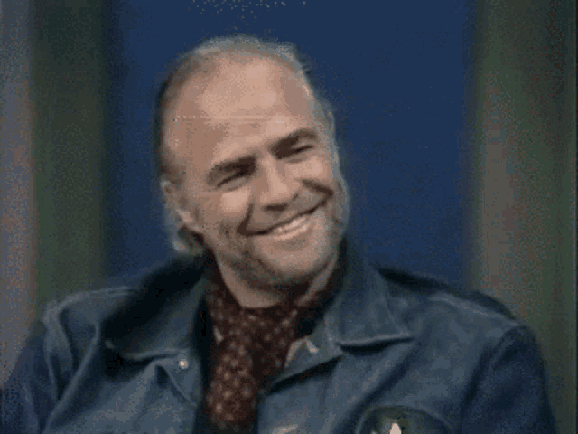 a man wearing a denim jacket and a scarf smiles