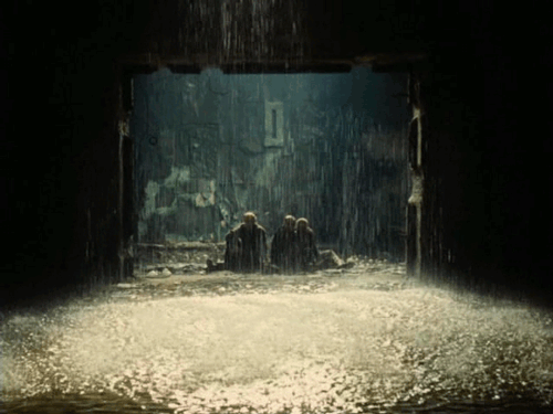 Three men sitting at the entrance to a room which is filled by pouring rain